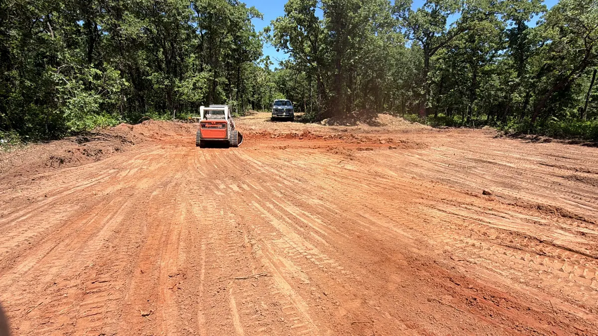 Track loader grading a freshly cleared red dirt pad in oak woods