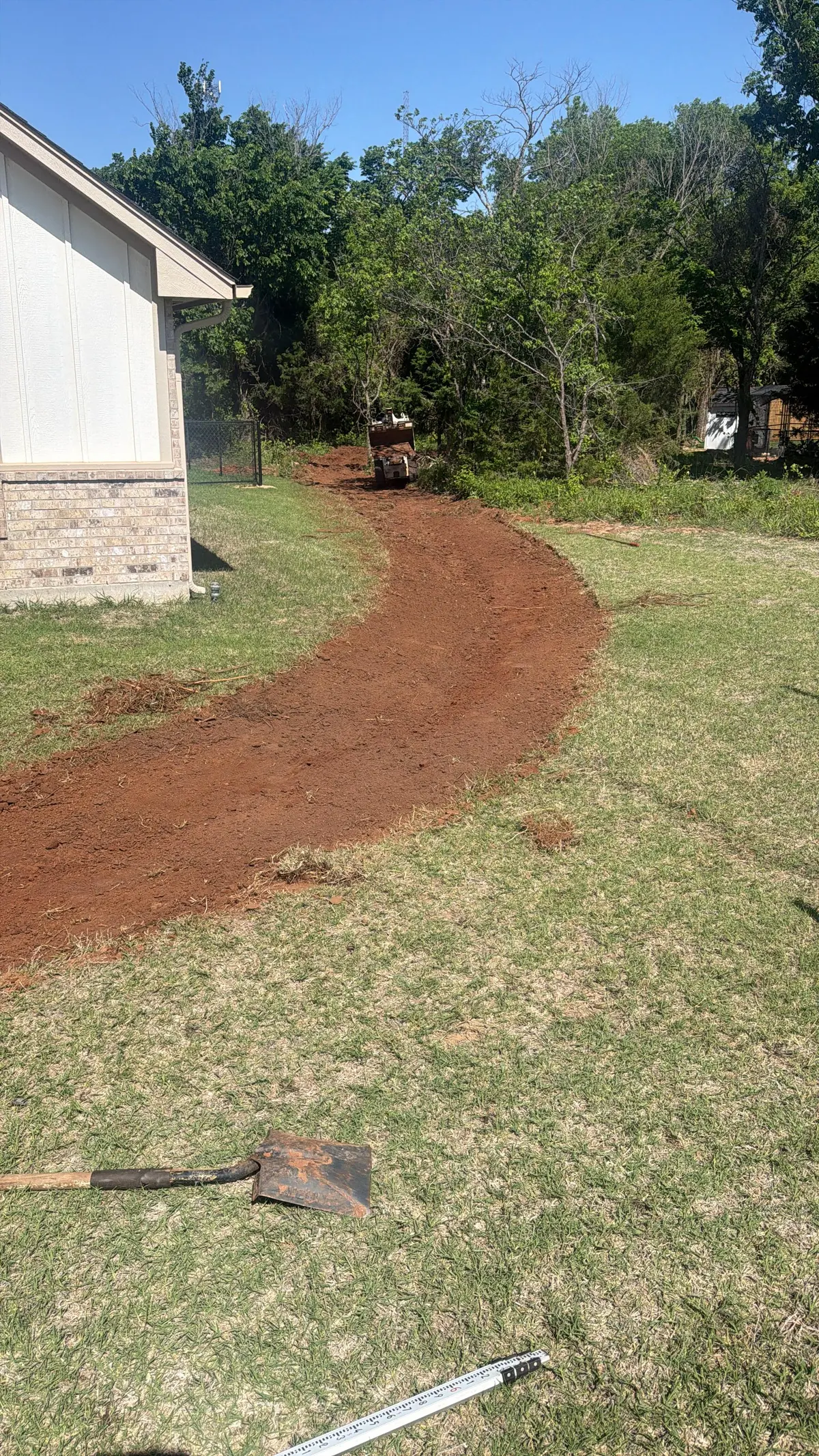 Graded drainage swale curving through a lawn with a compact roller working at the far end