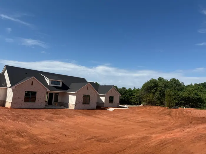 Finished grade around a new white brick farmhouse under a blue sky