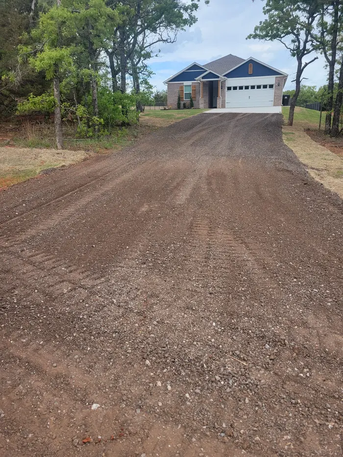 Fresh gravel driveway rising through oaks to a new home