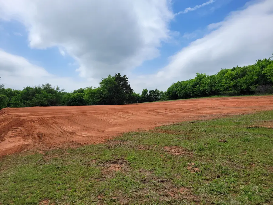 Wide freshly graded red dirt pad ringed by a green tree line